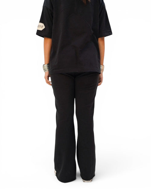 Thrive black pleated flared trousers in terry fabric with raw hem and elasticated drawstring waist, back view